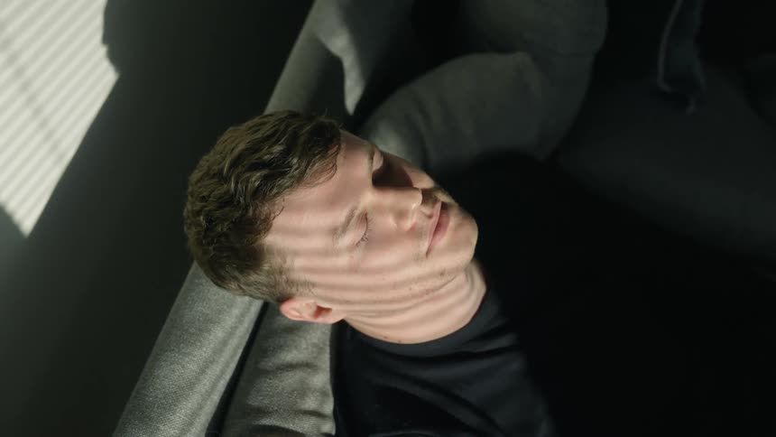 A man is resting on a couch near a window