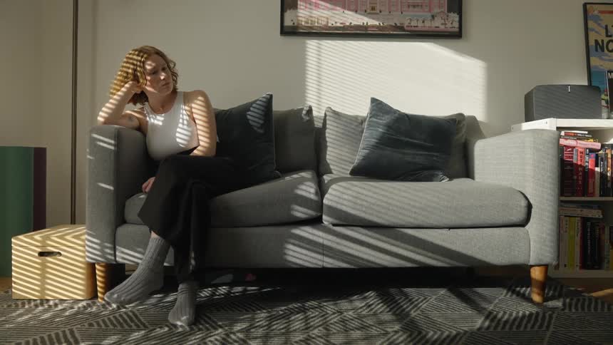 Young woman in deep thought thinking on the couch in the living room with sunlight shining through