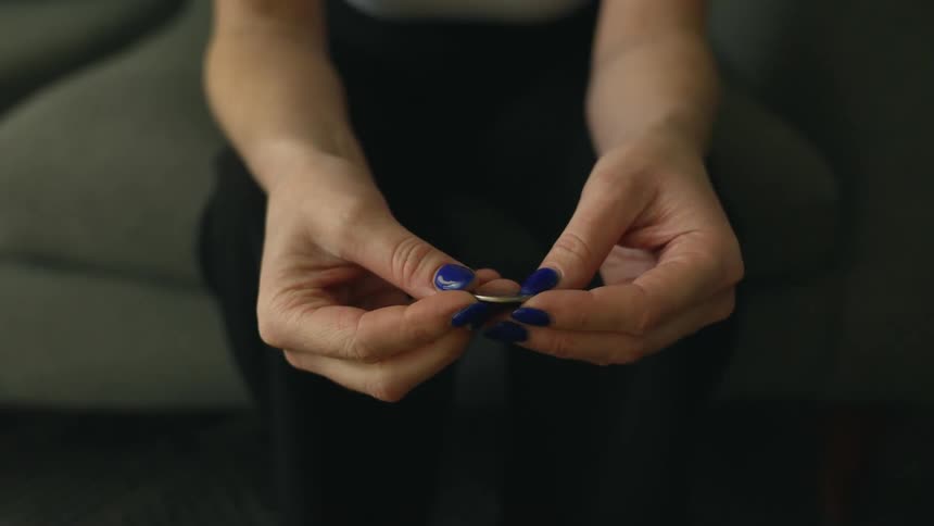 A woman is sitting on a couch running a quarter through her fingers