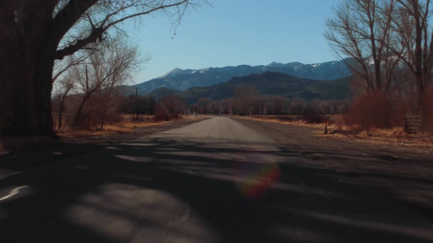 Moving down a rural road lined with bare trees and utility poles and mountains in the distance