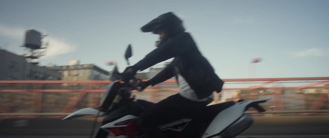 Man rides motorcycle along highway past apartment buildings
