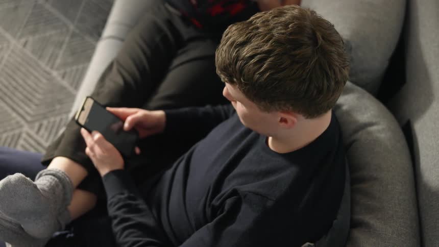 A man scrolls through his phone while his girlfriend sits with her feet in his lap