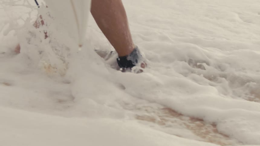 Bare feet walking through foamy water at the beach