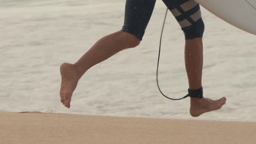 A man is running with a surf board and ankle leash and leaping into ocean water
