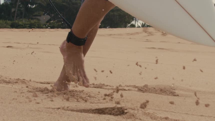 Surfer carrying surfboard and wearing ankle strap runs along beach under a fine rain
