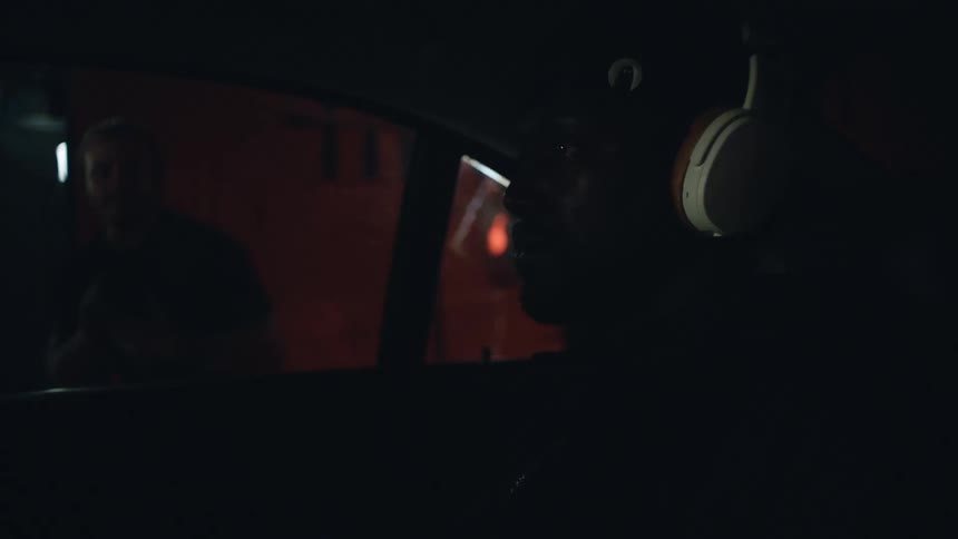 A man wears headphones and stares straight ahead in the backseat of a car as paparazzi outside take his photo