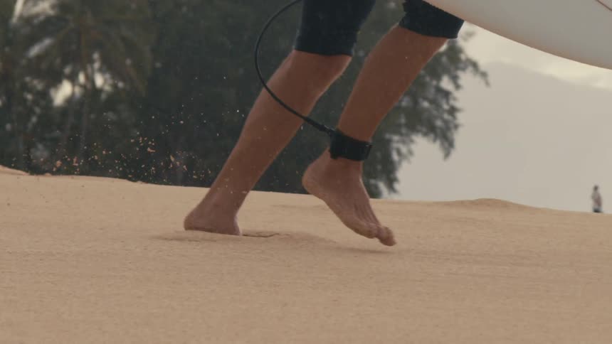 Bare feet running on the sand with a surfboard towards the ocean
