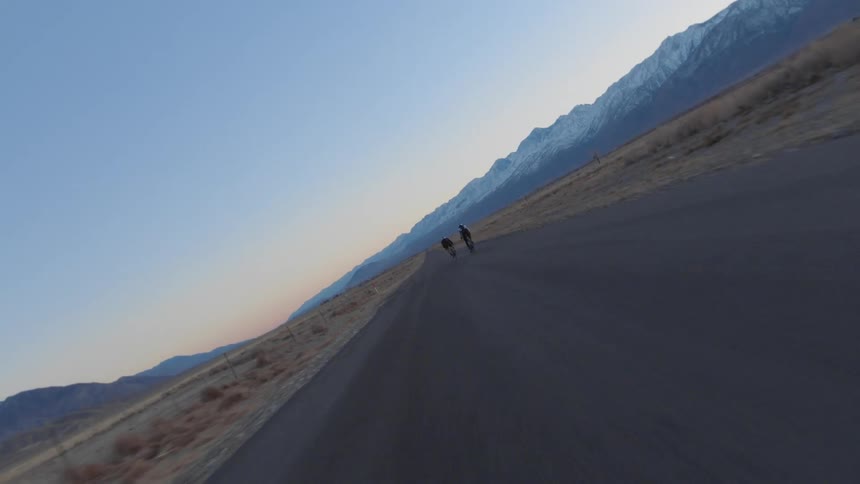 Cyclists cycle on country road with fields and distant snowy mountians in the background at dusk