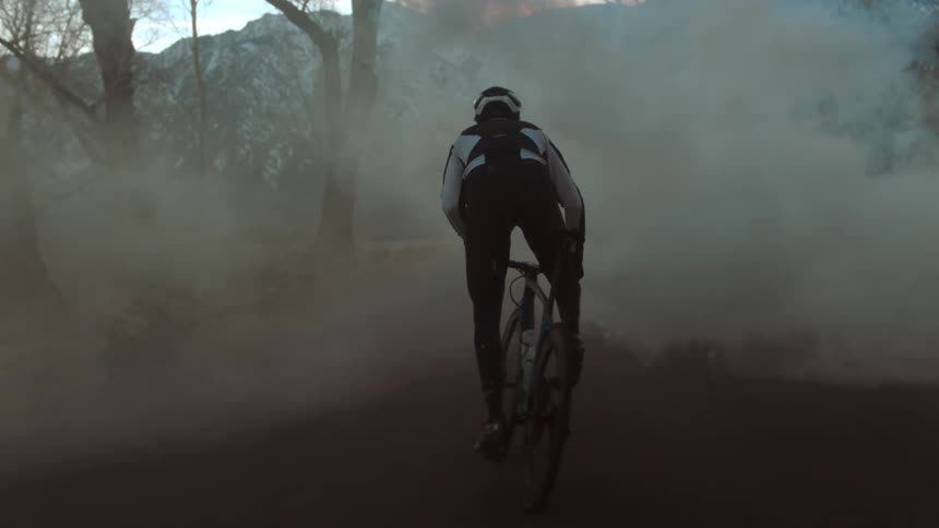 A cyclist pedals through smoke obscuring a road through the countryside during the day