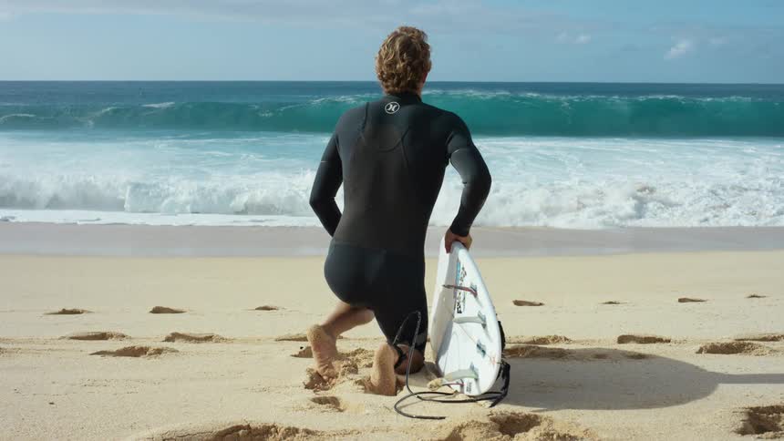 A man with a surfboard on the beach heading into the ocean