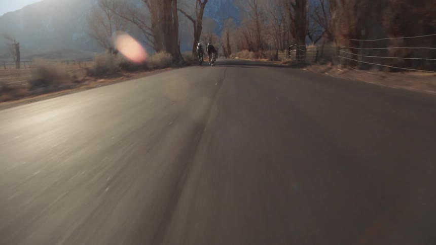Two cyclist ride bicycles on country road in the countryside with distant mountains in the background
