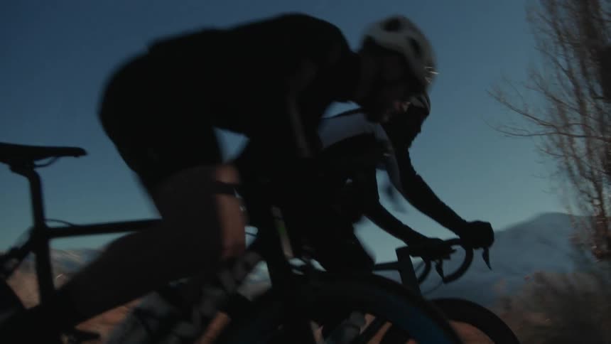 Two men riding bicycles on a road on the countryside at sunset