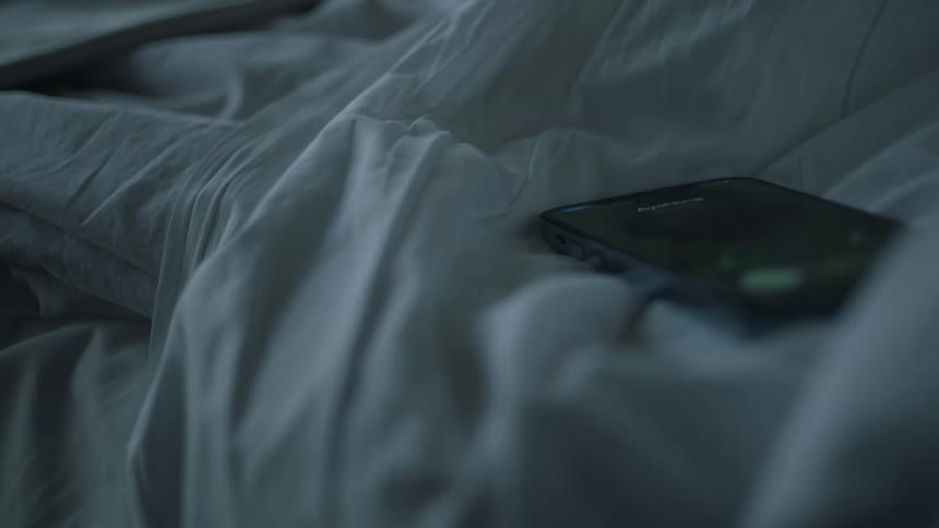 A cell phone is laying on bed sheets and it lights up when someone calls
