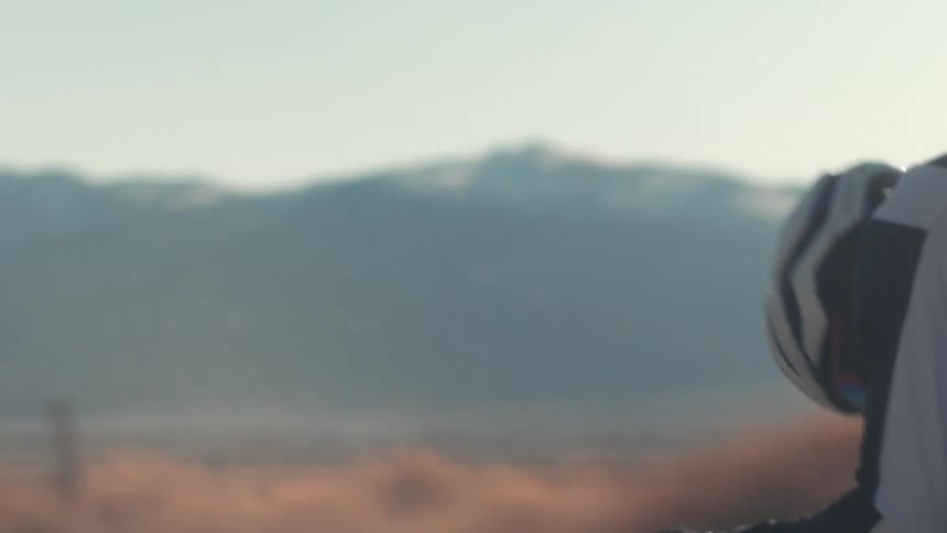 Man riding a bicycle on a road in the badlands near the mountains at sunset
