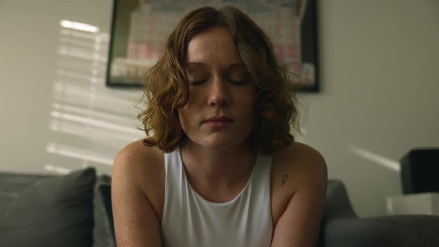 An unhappy woman sits on a sofa while lost in thought
