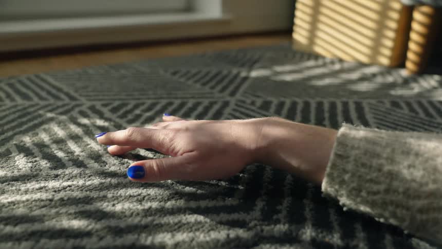 A woman taps her hand on a rug while sitting on the floor