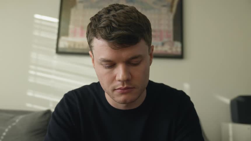 A man is sitting on a couch indoors during the daytime