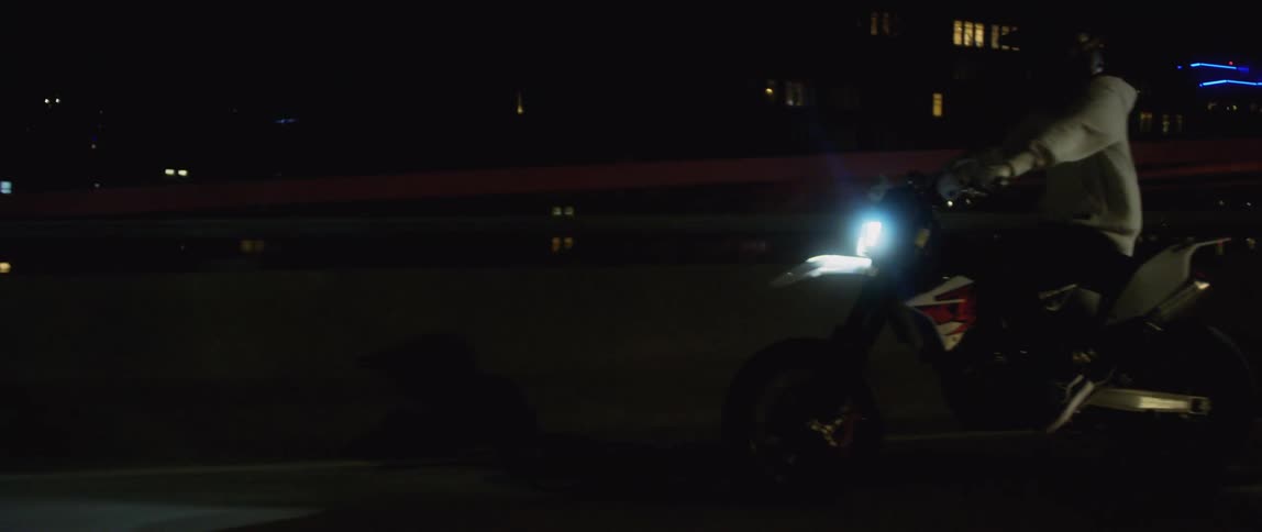 A person rides a motorcycle along a bridge through a metropolis at night