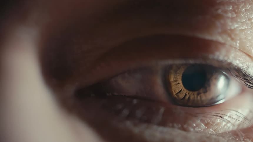 Extreme close up of a brown eye blinking from a light