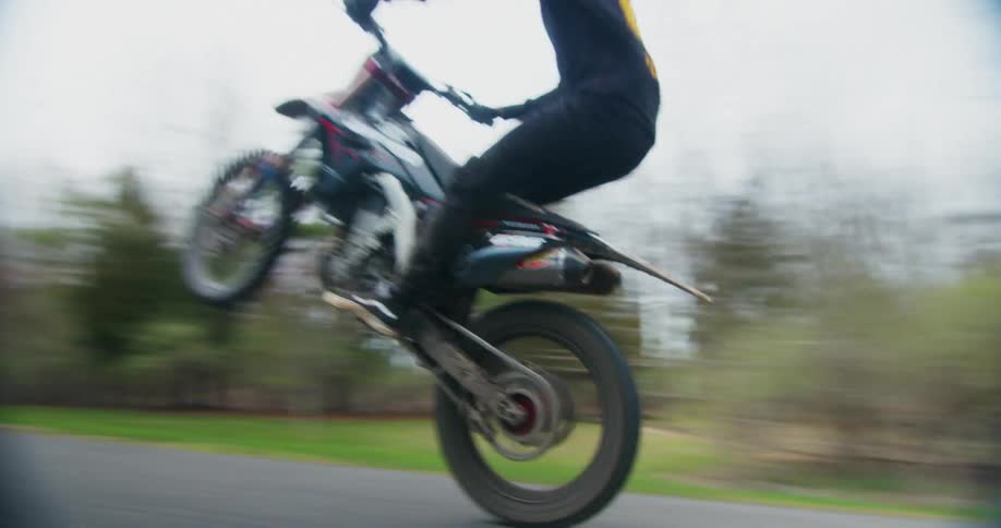 A motorcycle rider is riding a wheelie down a street