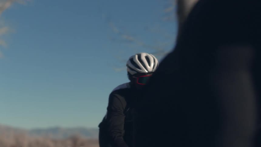A cyclist falls behind another while riding through the countryside on a clear day