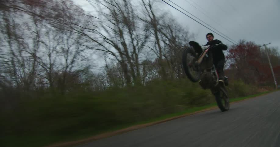A motorcycle rider is doing a wheelie down a street in the country