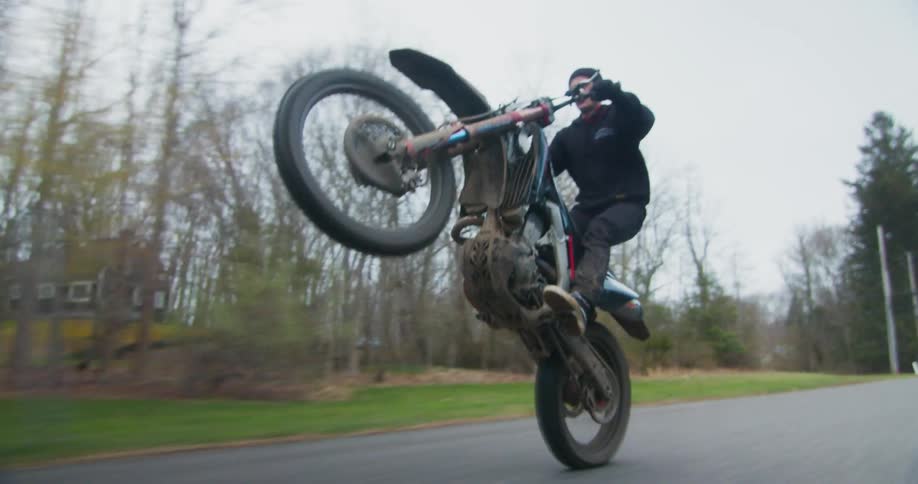 A motorcycle rider is popping a wheelie down a rural street