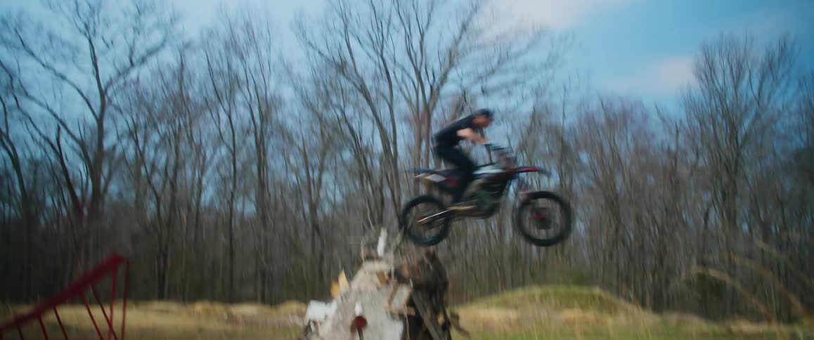 A man on a motorcycle uses a ramp to jump a pile of junk