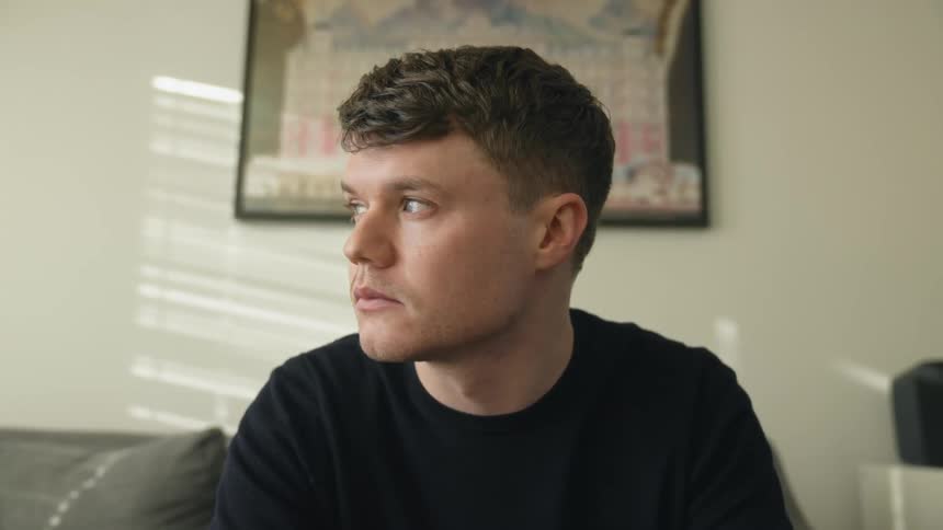 Pensive man with black t shirt sits on couch looking out the window
