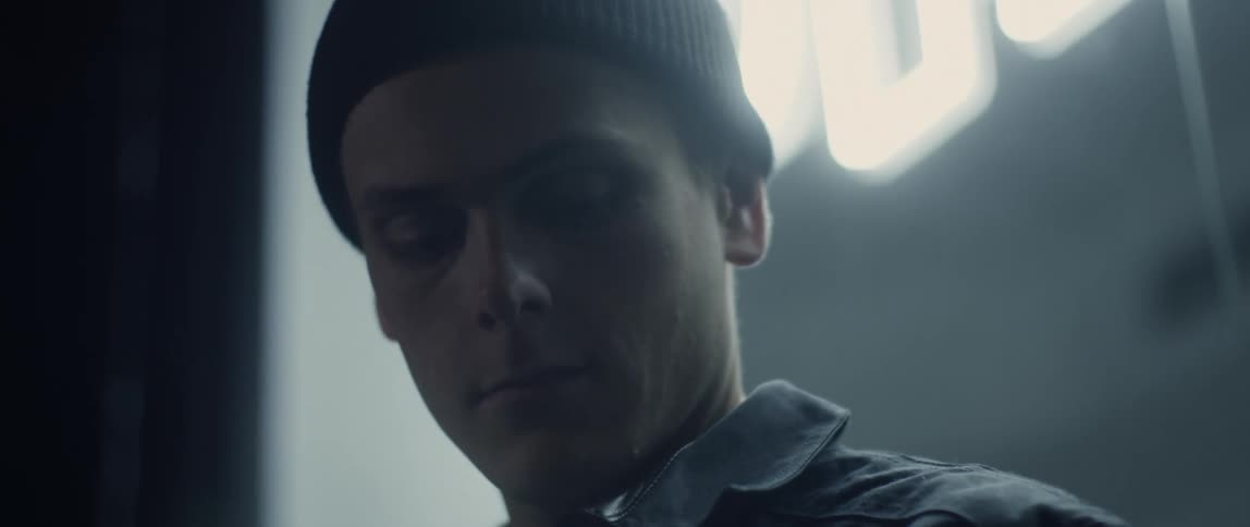 Young man wearing a black beanie standing in front of a neon store sign at night