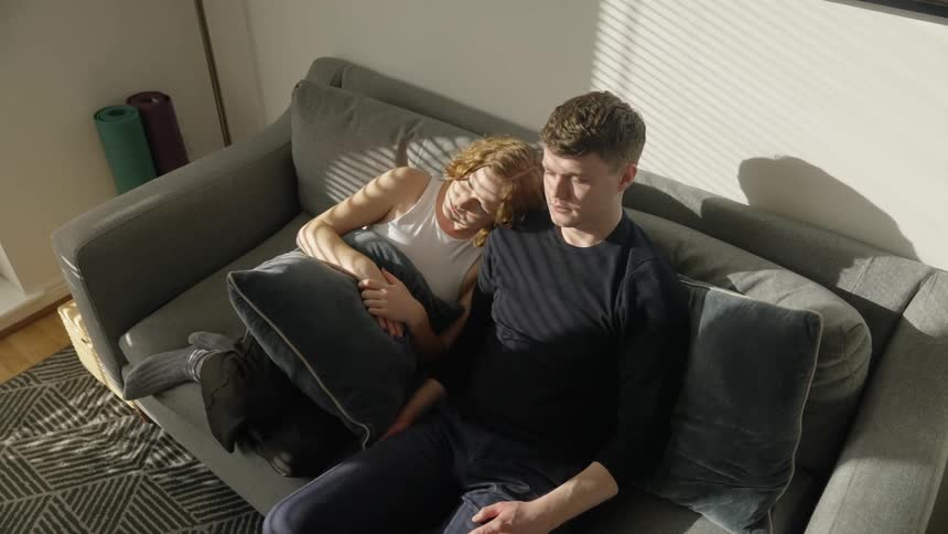 A woman lays her head on a mans shoulders as they sit on a couch together