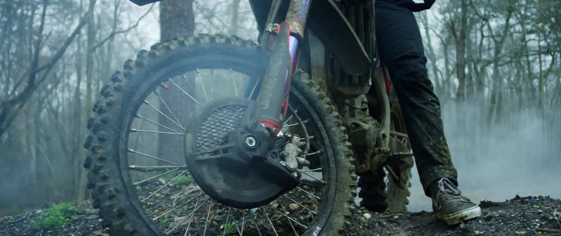 A man is sitting astride a dirt bike in a forest