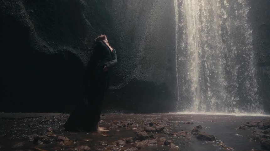 A woman standing in the cave by the waterfall whips her body around