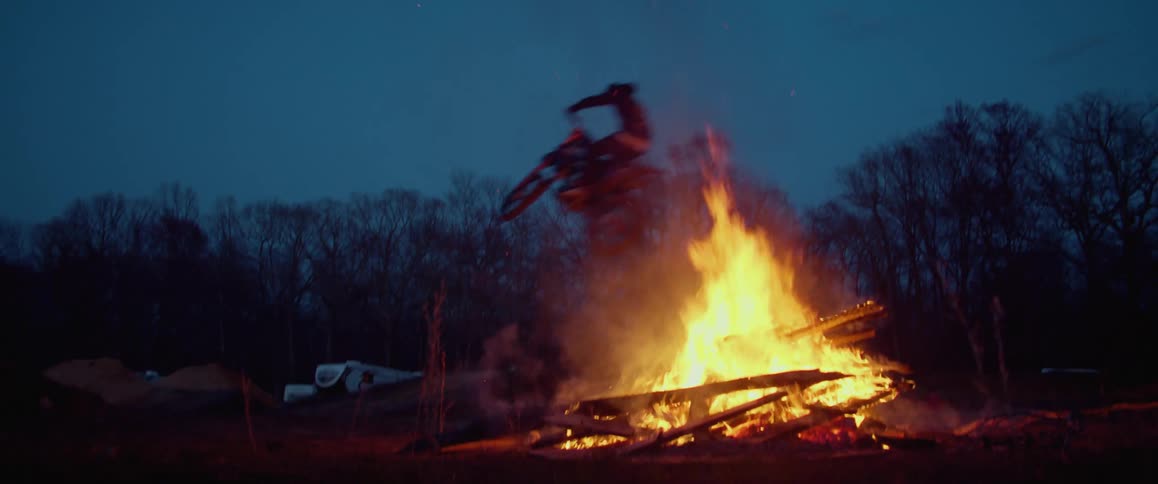 A person jumping over a large bonfire on a motorcycle at night