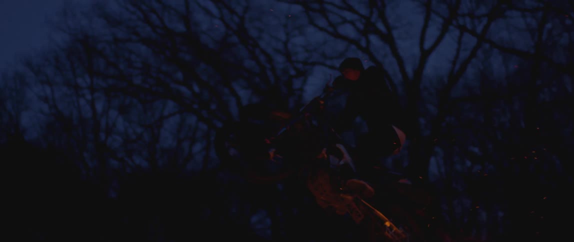 Motorcycle rider jumping over flames in the forest at night