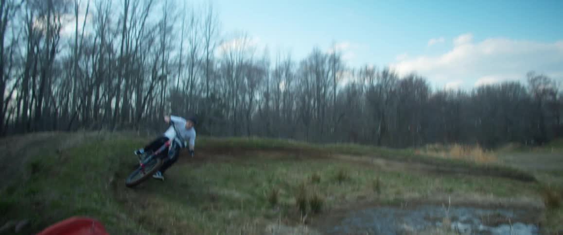 A man rides a motorcycle in circles around a puddle in a field