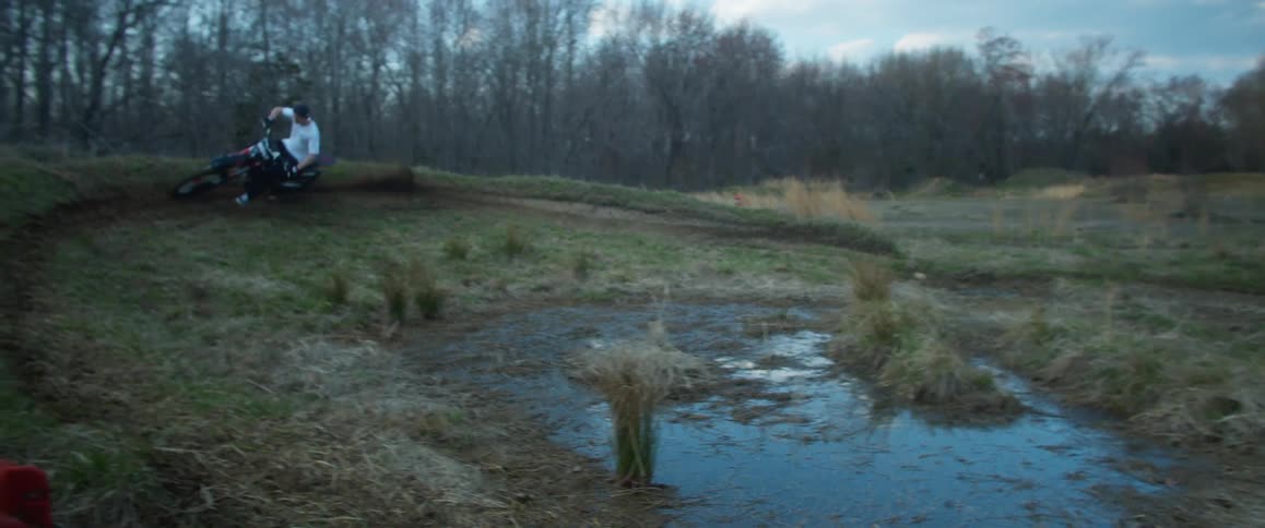 A man riding a dirt bike around a large mud puddle