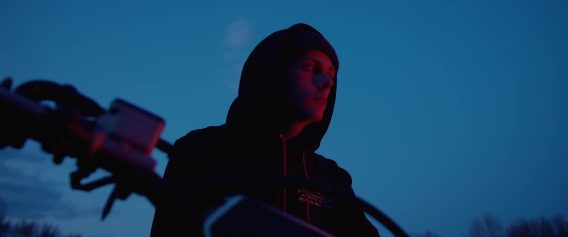 A man looks around while sitting on his parked motorcycle at dusk