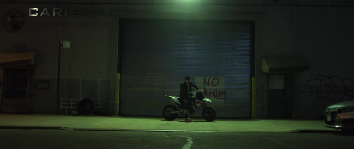 A man sits on his motorcycle in front of a no parking sign outside a warehouse