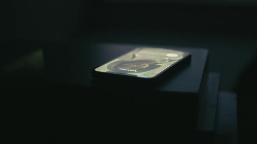 The lock screen of a smartphone lying on a table in a dark room changes as it recieves an incoming call