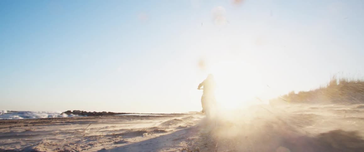 Silhouette of a man starting a motorcycle on the sand next to the beach at sunset