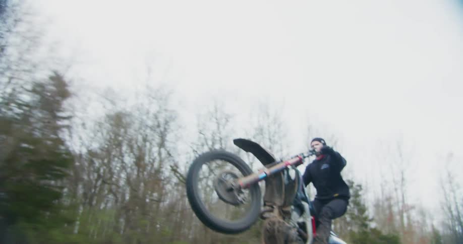 Young man doing stunts while driving a fast motorcycle on a road near a forest