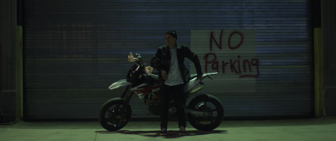 A man stands by his motorcycle in front of a no parking sign