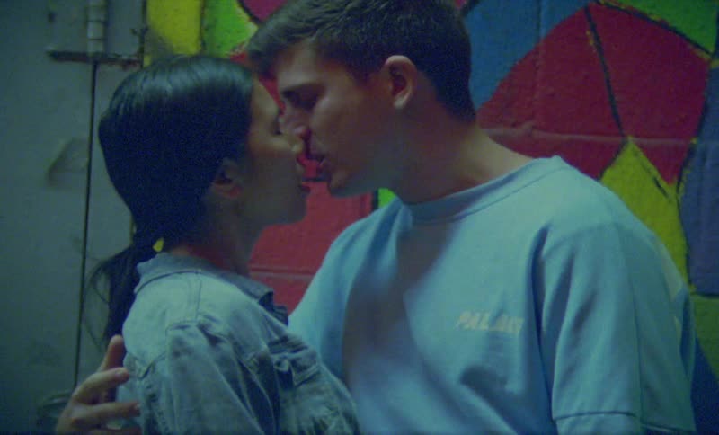 Couple stands kissing near brick wall decorated with mural
