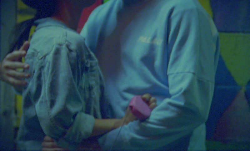 A teenage girl holds a dog on a leash as she stands outside kissing a teenage boy