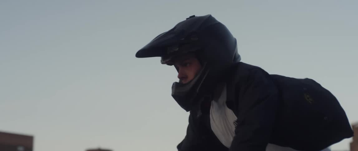 A teenager is riding a motor bike so fast that his coat is flying behind him