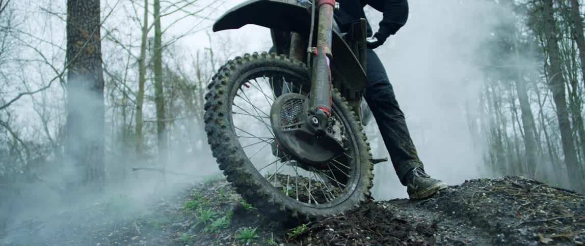 A person sits on a dirt bike in a forest as fog rolls by