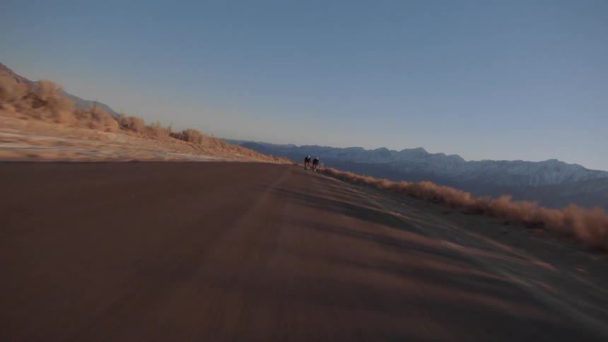 Twisting footage of two cyclist riding bicycles on a road through the badlands at sunset