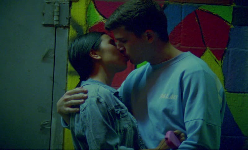 A couple make out outdoors in front of a mural