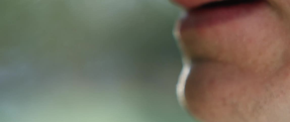 A man is smoking a blunt and blows smoke out from his nose and mouth